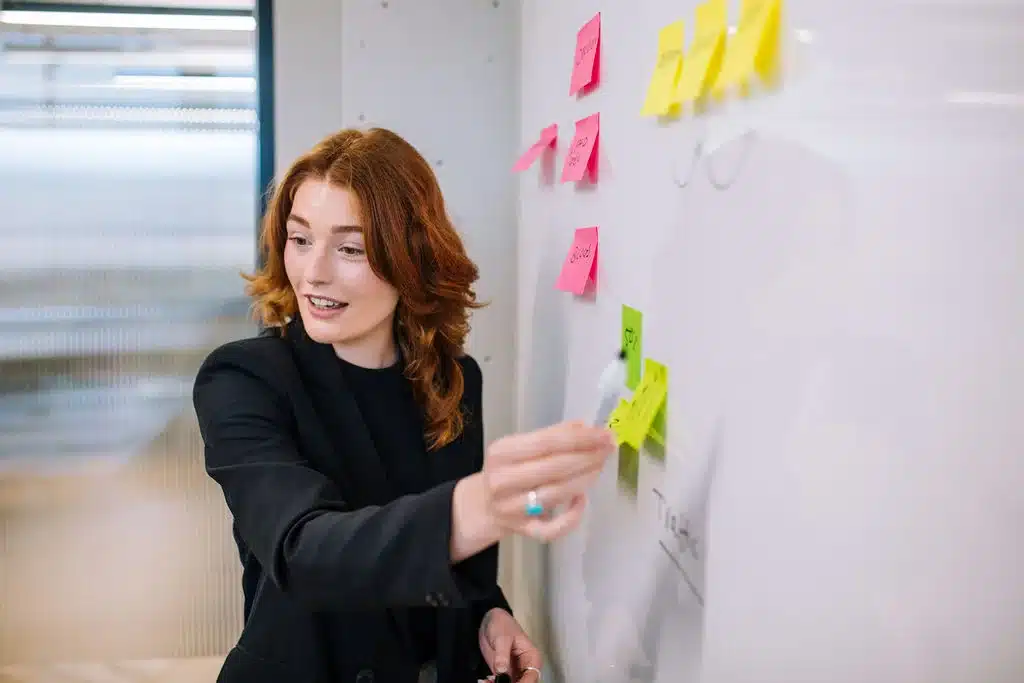 Businesswoman pointing at a whiteboard with post it notes on